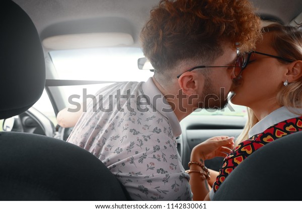 Beautiful young couple kissing on\
front seat of the car. Love is in the air. Back view. Young man\
embracing and kissing his beautiful girlfriend while on a road\
trip.