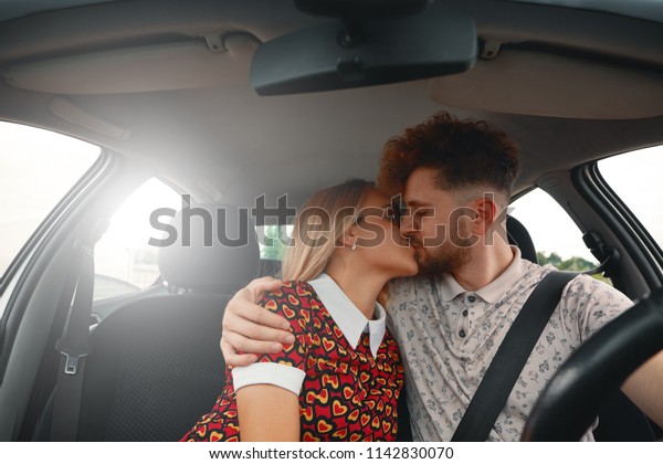 Beautiful young couple\
kissing on front seat of the car. Love is in the air. Front view.\
Young man embracing and kissing his beautiful girlfriend while on a\
road trip.