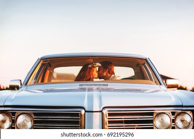 Beautiful young couple kissing while sitting together in an old retro car. Front window view