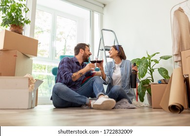 Beautiful young couple in love celebrating moving in new apartment, making a toast with glasses of wine