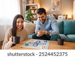 Beautiful young couple in love having fun playing ludo board game and drinking coffee while relaxing and enjoying leisure time together at home