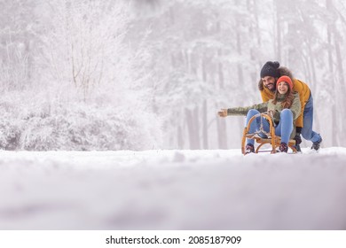 Schönes, verliebtes Paar, das sich auf einen Winterurlaub in den Bergen vergnügt, Freund, der die Freundin auf einem Schlitten schiebt, schneebedeckte, neblige Wintertage im Freien
