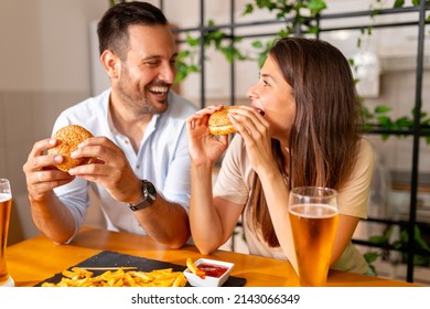 Beautiful young couple in love having fun spending leisure time together at home, eating burgers and drinking beer - Powered by Shutterstock