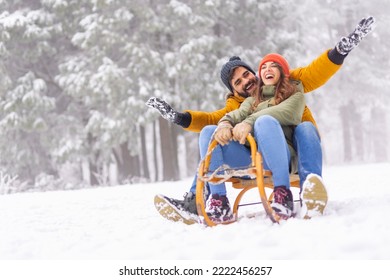 Beautiful young couple in love having fun sledging while spending winter vacation in mountains, enjoying snowy day outdoors
