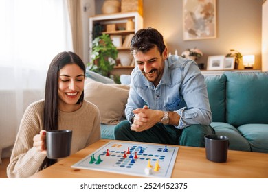 Beautiful young couple in love having fun playing ludo board game and drinking coffee while relaxing and enjoying leisure time together at home - Powered by Shutterstock