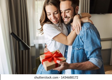 Beautiful Young Couple In Love At Home, Celebrating With A Gift Box Exchange, Hugging