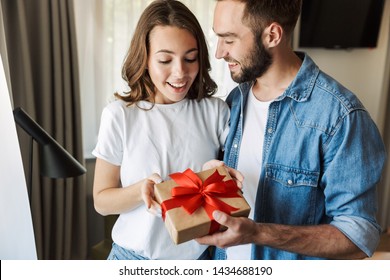 Beautiful Young Couple In Love At Home, Celebrating With A Gift Box Exchange