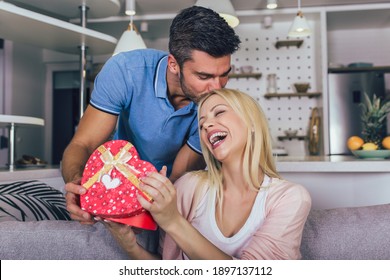 Beautiful Young Couple In Love At Home, Celebrating With A Gift Box Exchange