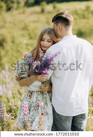 Beautiful young couple in love on a blooming field with a bouquet of bright lupine flowers
