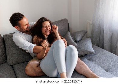 Beautiful young couple in love relaxing at home, hugging, tickling and laughing on the couch