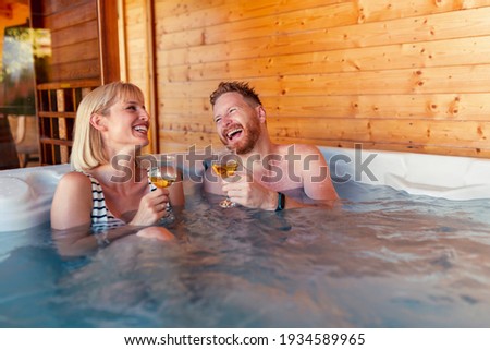 Beautiful young couple in love relaxing and drinking wine in a hotel resort spa center hot tub, having fun while on a vacation