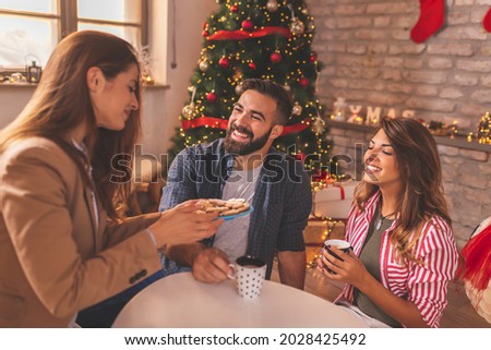 Beautiful young couple in love spending Christmas day with friends at home, drinking coffee, eating Christmas cookies and having fun
