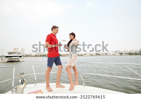 Beautiful young couple in love standing on yacht bow and drinking champagne enjoying romantic date