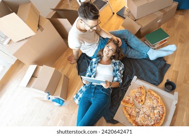 Beautiful young couple in love using digital tablet pc shopping online in new family home while taking a break from moving-in and having a pizza. - Powered by Shutterstock