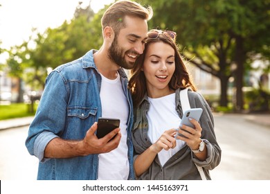 Beautiful young couple in love walking outdoors at the city street, using mobile phones - Powered by Shutterstock