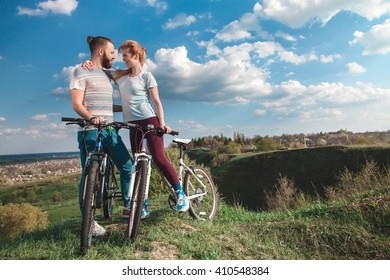 Beautiful young couple in love walking with bicycles hugging and looking at each other. The concept of joy and happiness