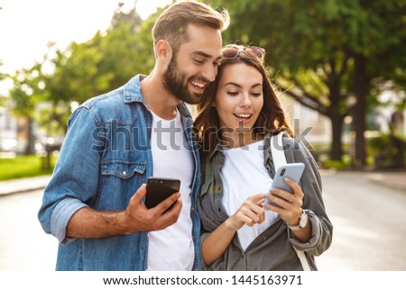 Beautiful young couple in love walking outdoors at the city street, using mobile phones