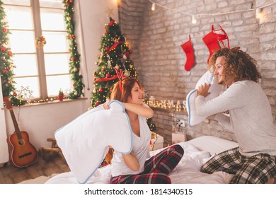 Beautiful Young Couple In Love Wearing Pajamas, Having A Pillow Fight In Bed On Christmas Morning, Having Fun At Home During Winter Holiday Season