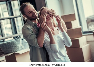 Beautiful Young Couple Is Moving Into New Apartment. Guy Is Covering His Girlfriend's Eyes Making A Surprise