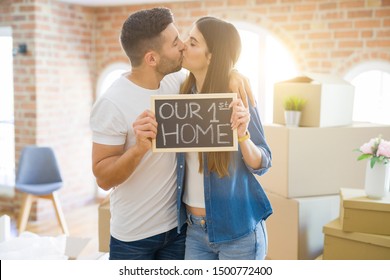 Beautiful young couple moving to a new house, smiling very happy holding blackboard with our first home text స్టాక్ ఫోటో