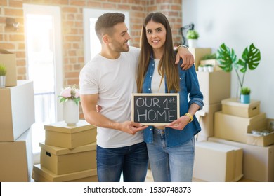 Beautiful young couple moving to a new house, smiling very happy holding blackboard with our first home text