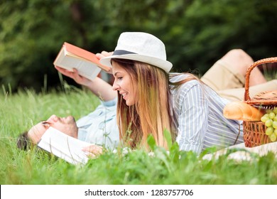 Beautiful young couple relaxing in city park, reading books while lying on a picnic blanket