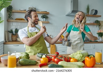 Beautiful young couple singing and having fun while cooking together at the kitchen - Powered by Shutterstock