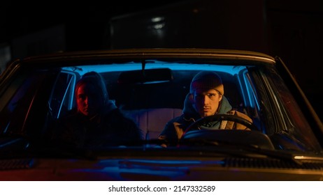 Beautiful Young Couple Sitting In Awkward Silence In A Vintage Looking Car With Neon Lights Surrounding Them And A Street Light Hitting The Man's Face In An Artistic Way. Looking At The Distance.