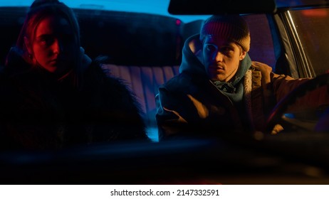 Beautiful Young Couple Sitting In Awkward Silence In A Vintage Looking Car With Neon Lights Surrounding Them And A Street Light Hitting The Man's Face In An Artistic Way. Guy Looking At Girl.