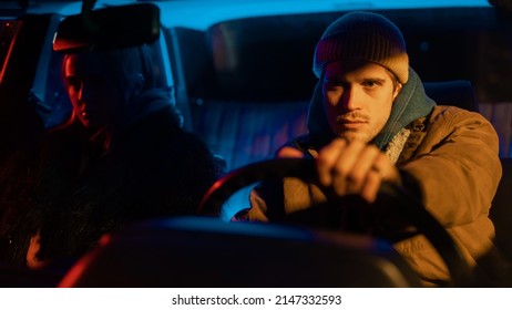 Beautiful Young Couple Sitting In Awkward Silence In A Vintage Looking Car With Neon Lights Surrounding Them And A Street Light Hitting The Man's Face In An Artistic Way.