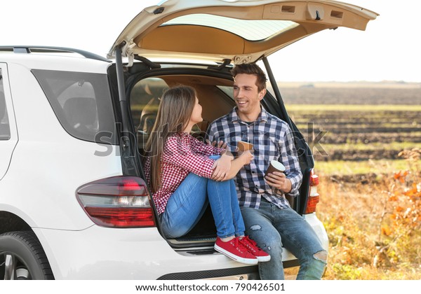 Beautiful\
young couple sitting with coffee in car\
trunk