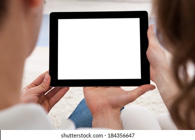 Beautiful young couple sitting side by side on a sofa looking at a tablet together - Powered by Shutterstock