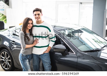 Beautiful young couple standing at the car dealership and making their decision