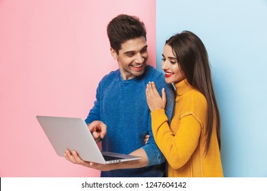 Beautiful Young Couple Standing Isolated Over Two Colored Background, Using Laptop Computer