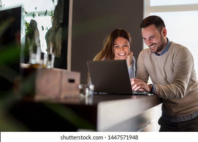 Beautiful Young Couple Standing Next To A Restaurant Counter, Using A Laptop Computer