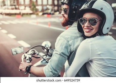 Beautiful young couple in sun glasses and helmets is smiling while riding a scooter - Powered by Shutterstock