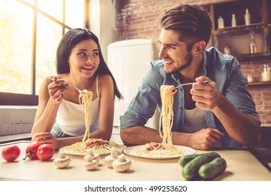 Beautiful young couple is talking, looking at each other and smiling while eating in kitchen at home