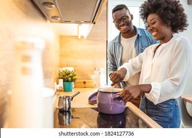 Beautiful young couple is talking and smiling while cooking healthy food in kitchen at home. Romantic couple is cooking on kitchen. Handsome man and attractive young woman are having fun together - Powered by Shutterstock