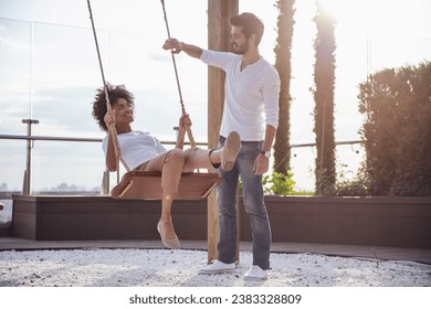 Beautiful young couple is talking and smiling while resting outdoors, girl is swinging