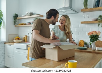 Beautiful young couple unpacking box and smiling while standing at the domestic kitchen  - Powered by Shutterstock