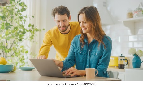 Beautiful Young Couple Using Laptop Computer in Kitchen at Home. Female Working on a Project. Boyfriend is Helping Girlfriend with Online Work. Female Browsing Internet and Doing Online Shopping. - Powered by Shutterstock