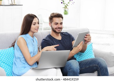 Beautiful young couple using laptop and tablet at home