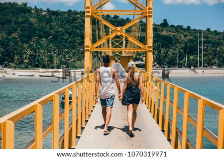 beautiful young couple walking along the yellow bridge across the river, couple follow me in island, Woman wanting her man to follow her in vacation or honeymoon to beach by the ocean, love, hair wild