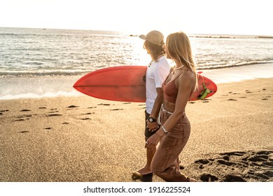 Beautiful young couple walking on the sandy beach during sunset and looking at the ocean. Man carrying surf board.  Island vibes. Summer lifestyle.  - Powered by Shutterstock