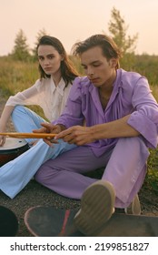 Beautiful young couple is walking on the road. Hobbies. Musicians and skaters. Girl and boy. Active lifestyle. Stylish people in retro clothes. Suburb area. Summer landscape, sunset. Colorful. - Shutterstock ID 2199851827