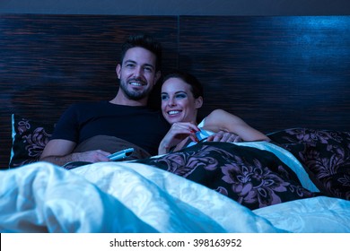 Beautiful Young Couple Watching TV In Bed At Night.