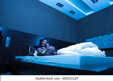 Beautiful Young Couple Watching TV In Bed At Night.