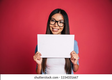 Beautiful young cute lovely asian woman in glasses with white blank board or banner in hands for advertisement over pink background - Powered by Shutterstock