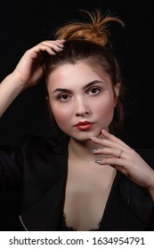 Beautiful Young Dark-haired Girl With Brown Eyes In Dark Clothes. Low Key Portrait On A Dark Background. The Face Of The Model Is Lit By Bright Light. Close-up Portrait Of A Hand In A Frame.