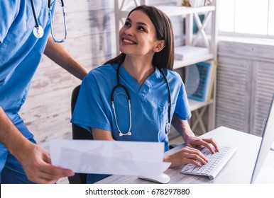 Beautiful young doctors are using a computer, discussing documents and smiling while working in office